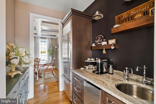 bar featuring dark brown cabinetry, coffered ceiling, sink, light wood-type flooring, and appliances with stainless steel finishes