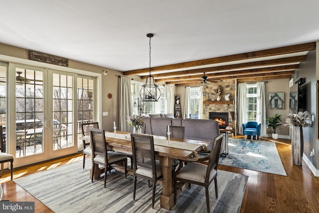 dining room with hardwood / wood-style floors, a stone fireplace, french doors, and beamed ceiling