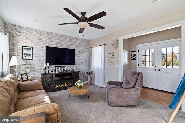 living room featuring french doors, ceiling fan, brick wall, and hardwood / wood-style floors