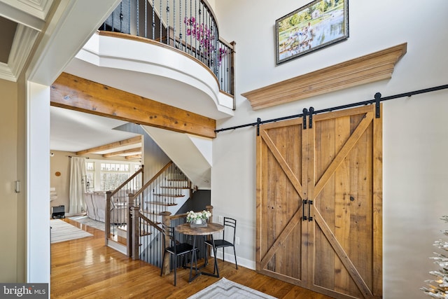 foyer entrance featuring hardwood / wood-style flooring, a barn door, a towering ceiling, and beam ceiling