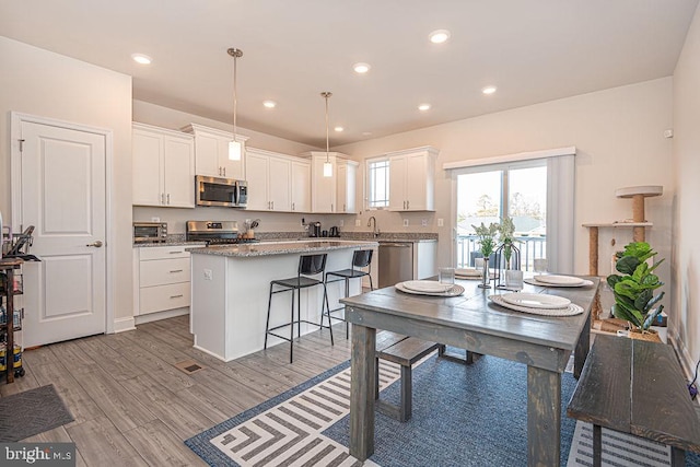 kitchen with a kitchen island, white cabinets, hanging light fixtures, light hardwood / wood-style floors, and stainless steel appliances