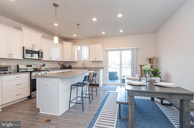 kitchen featuring pendant lighting, stainless steel appliances, a kitchen island, and white cabinets