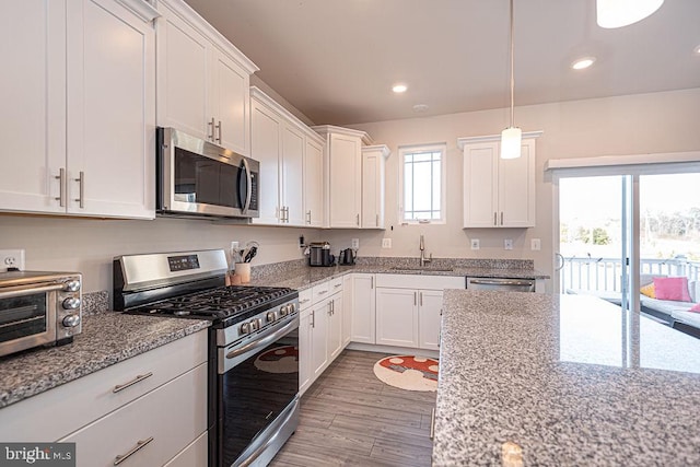 kitchen with sink, white cabinetry, light stone counters, light hardwood / wood-style flooring, and appliances with stainless steel finishes