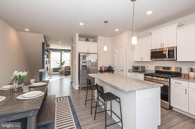 kitchen featuring stainless steel appliances, decorative light fixtures, a center island, and white cabinets