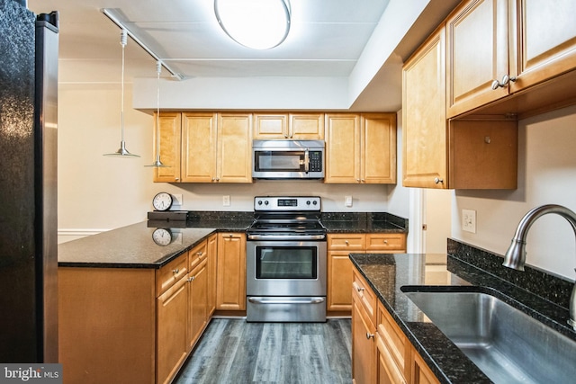 kitchen featuring dark stone countertops, dark wood-style flooring, hanging light fixtures, stainless steel appliances, and a sink