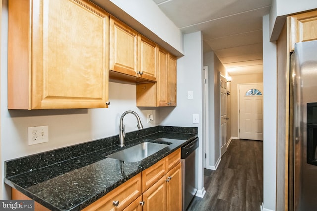 kitchen featuring stainless steel appliances, a sink, baseboards, dark stone countertops, and dark wood finished floors