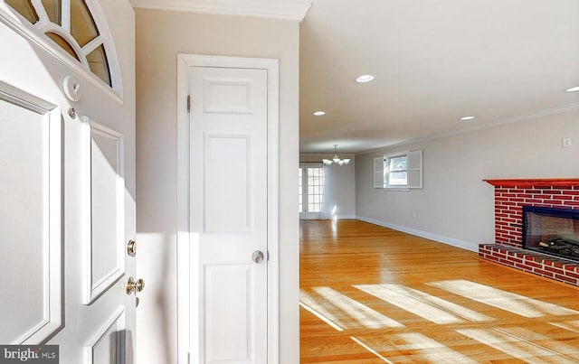 interior space featuring crown molding, a brick fireplace, hardwood / wood-style flooring, and an inviting chandelier