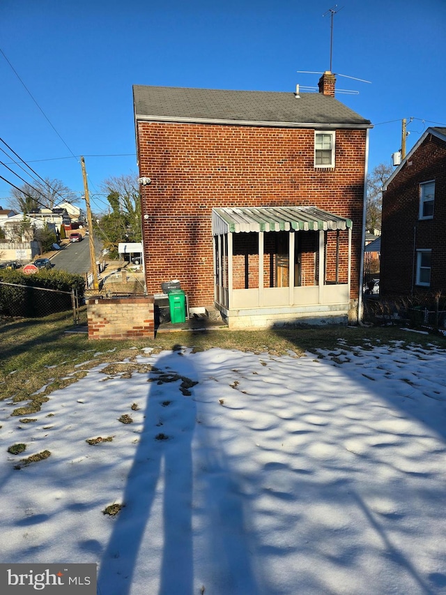 snow covered rear of property with a sunroom