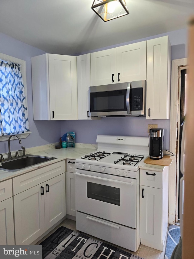 kitchen with white cabinetry, white range with gas cooktop, refrigerator, and sink