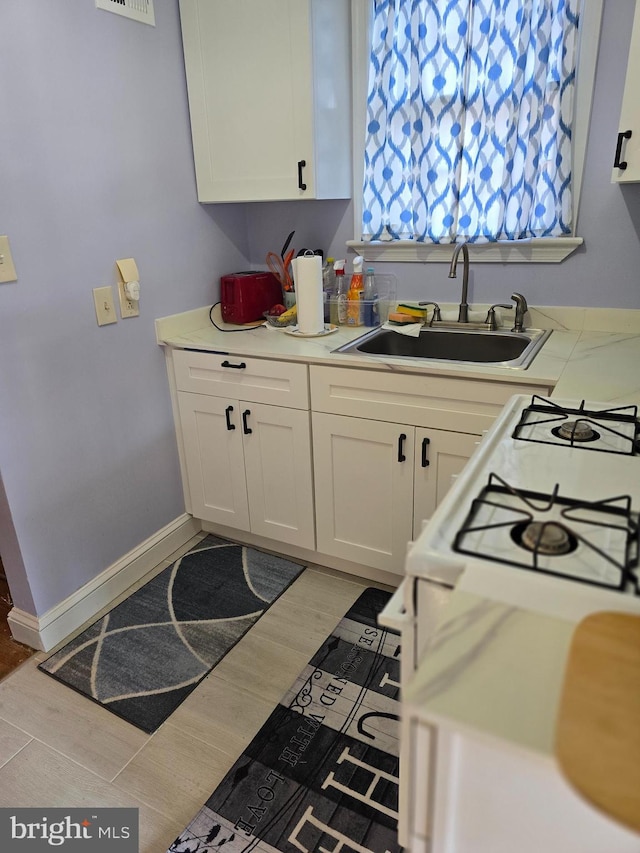 kitchen with white cabinetry, sink, white gas stove, and light hardwood / wood-style flooring