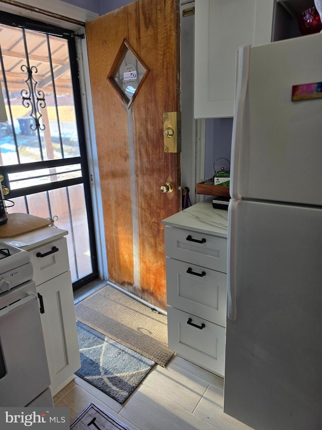 kitchen with white cabinetry, light stone counters, and white appliances