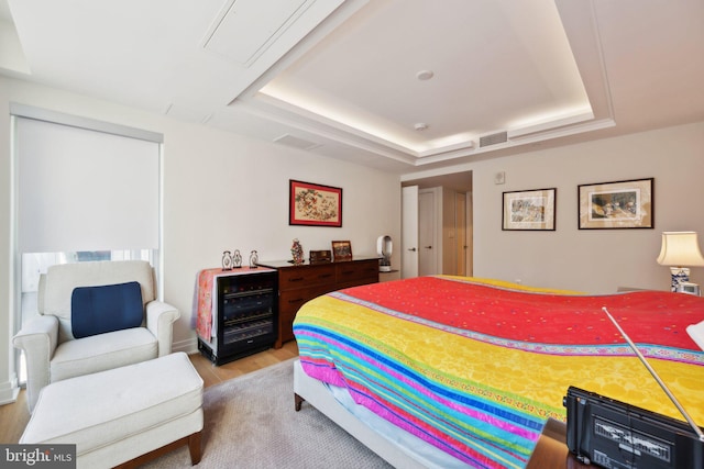 bedroom featuring light wood-style floors, a tray ceiling, and visible vents