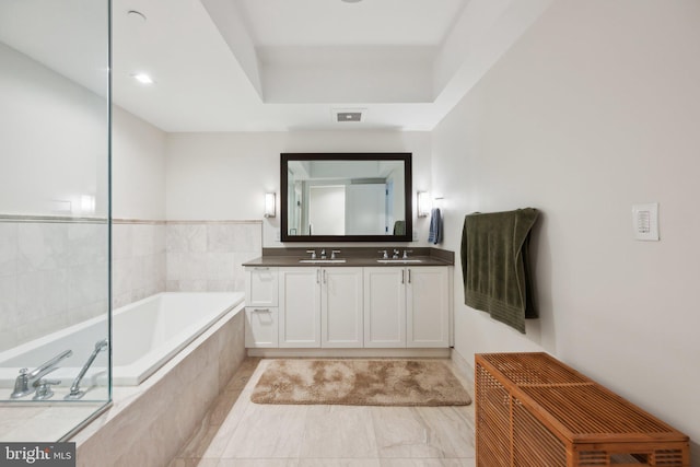 bathroom featuring a tray ceiling, a garden tub, a sink, and double vanity