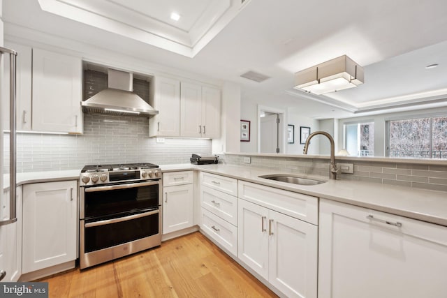 kitchen with a sink, white cabinets, light countertops, wall chimney range hood, and double oven range