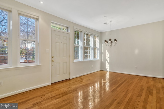 foyer entrance with light wood-type flooring, a wealth of natural light, and an inviting chandelier