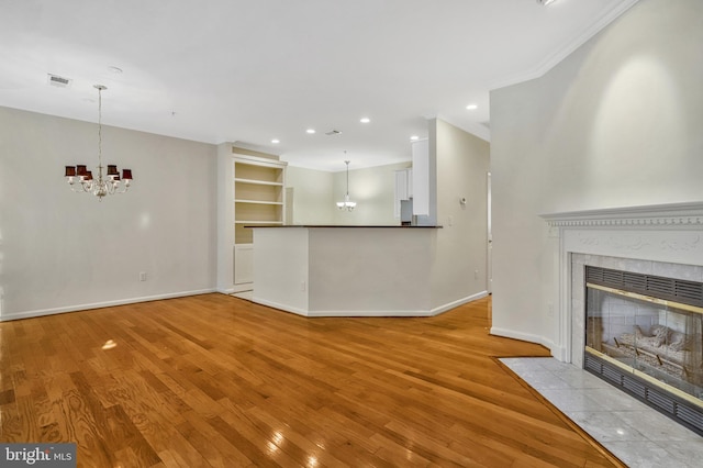 unfurnished living room featuring ornamental molding, a chandelier, a tile fireplace, and light hardwood / wood-style flooring