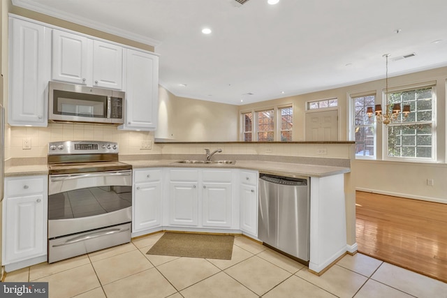 kitchen featuring sink, appliances with stainless steel finishes, white cabinets, decorative light fixtures, and kitchen peninsula