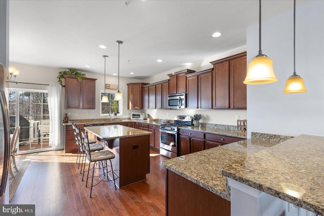 kitchen featuring a kitchen island, appliances with stainless steel finishes, stone countertops, a kitchen breakfast bar, and hanging light fixtures