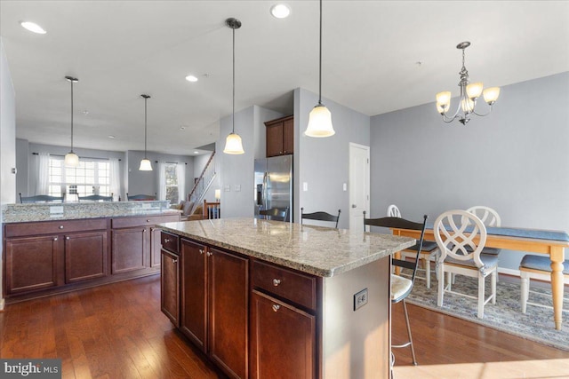 kitchen featuring stainless steel refrigerator with ice dispenser, a breakfast bar area, a center island, hanging light fixtures, and light stone countertops