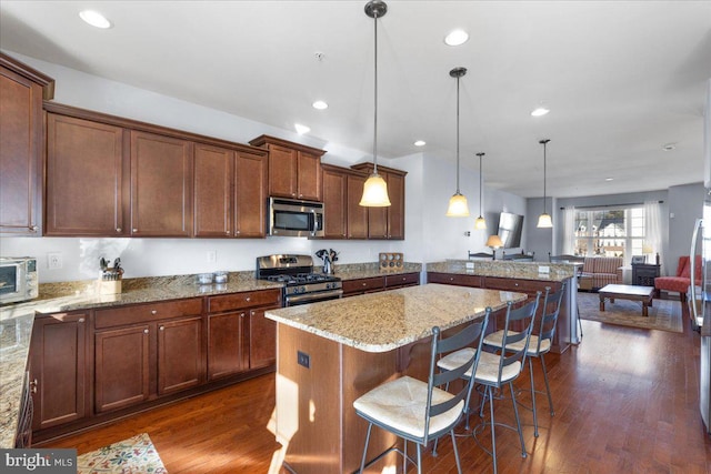 kitchen with a breakfast bar, hanging light fixtures, stainless steel appliances, light stone countertops, and a kitchen island