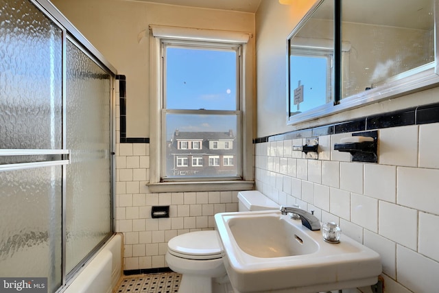 full bathroom with enclosed tub / shower combo, toilet, sink, and tile walls