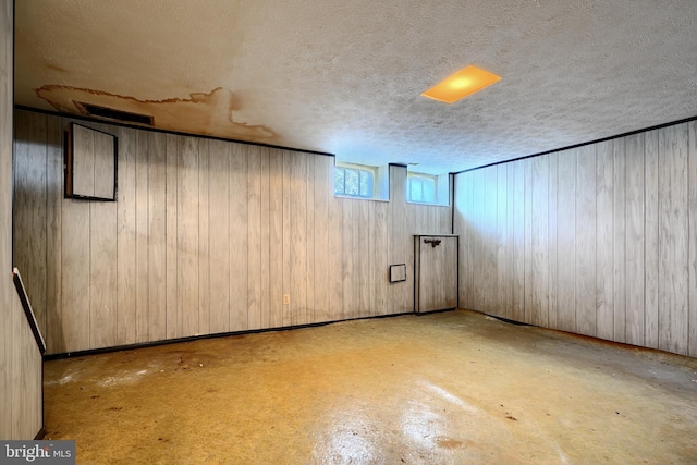 basement featuring a textured ceiling and wood walls