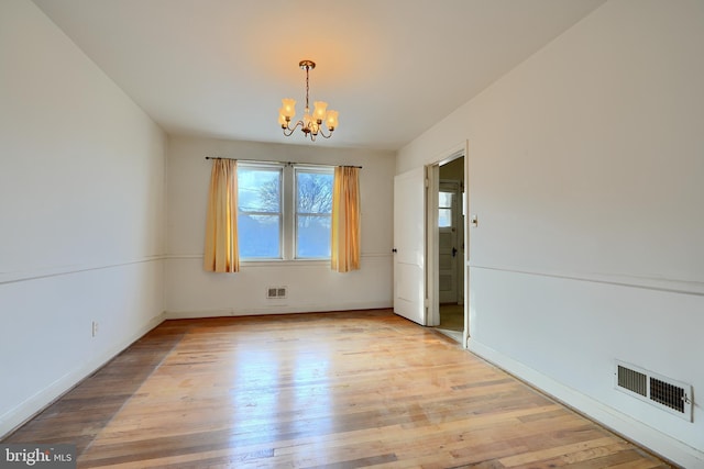 spare room with light hardwood / wood-style floors and a chandelier