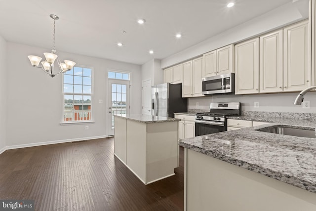 kitchen with light stone countertops, sink, stainless steel appliances, and hanging light fixtures