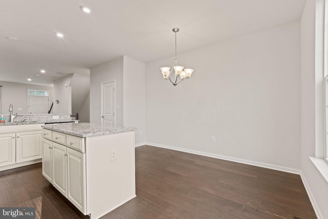 kitchen featuring a kitchen island, hanging light fixtures, a notable chandelier, light stone counters, and dark wood-type flooring