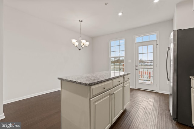 kitchen featuring dark wood-type flooring, stainless steel refrigerator, hanging light fixtures, a kitchen island, and a chandelier