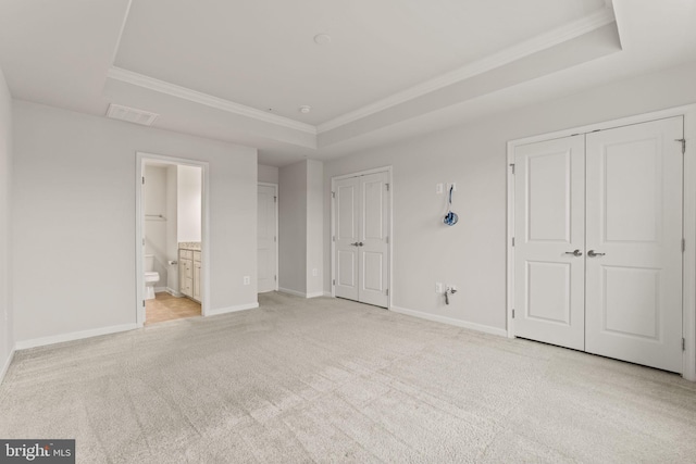 unfurnished bedroom with ensuite bathroom, light carpet, and a tray ceiling