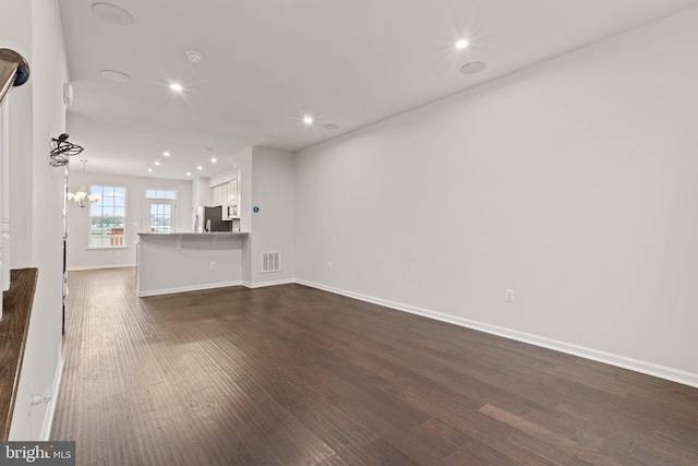 unfurnished living room with an inviting chandelier and dark hardwood / wood-style floors