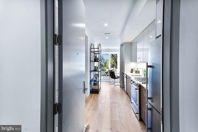 kitchen with white cabinetry, stainless steel appliances, sink, and light hardwood / wood-style flooring