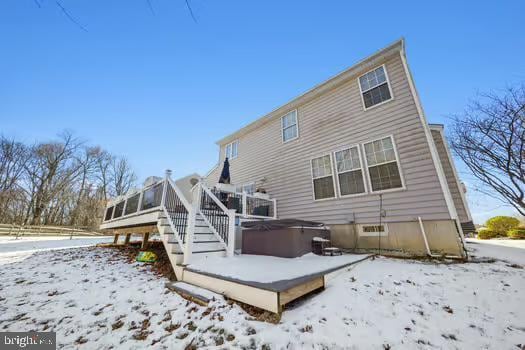 snow covered back of property with a hot tub, a deck, and a sunroom