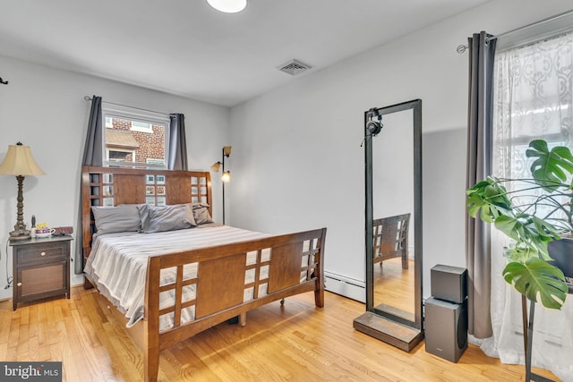 bedroom with a baseboard heating unit and light wood-type flooring