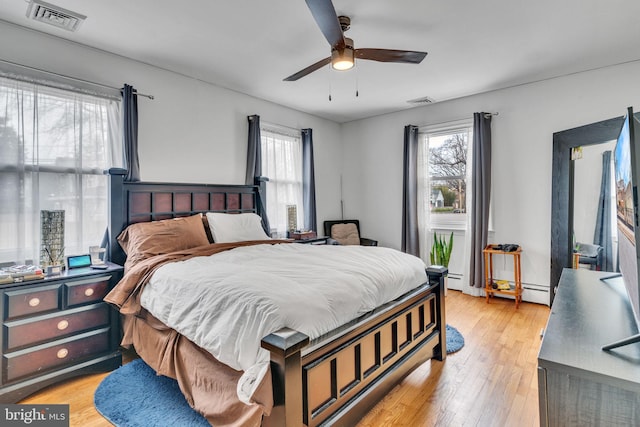 bedroom with ceiling fan, a baseboard radiator, light hardwood / wood-style floors, and multiple windows