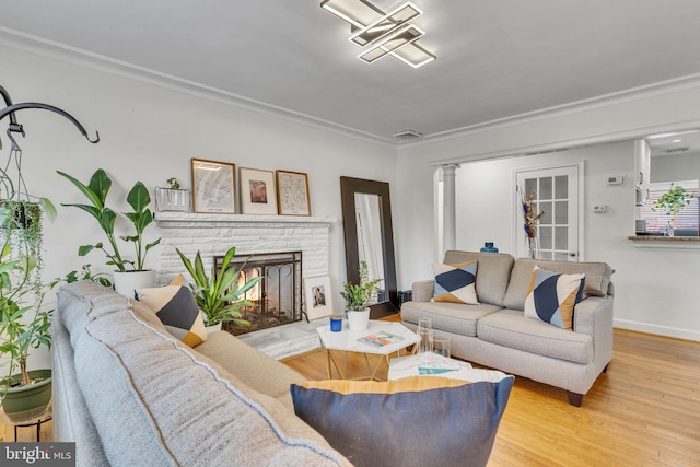 living room with crown molding, a stone fireplace, decorative columns, and light wood-type flooring