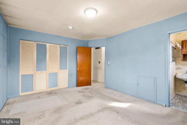 unfurnished bedroom with connected bathroom, sink, light colored carpet, and a closet