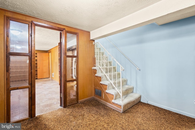 stairs with carpet flooring, wooden walls, and a textured ceiling