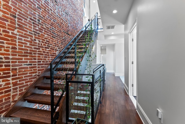 staircase with wood-type flooring, brick wall, and a towering ceiling