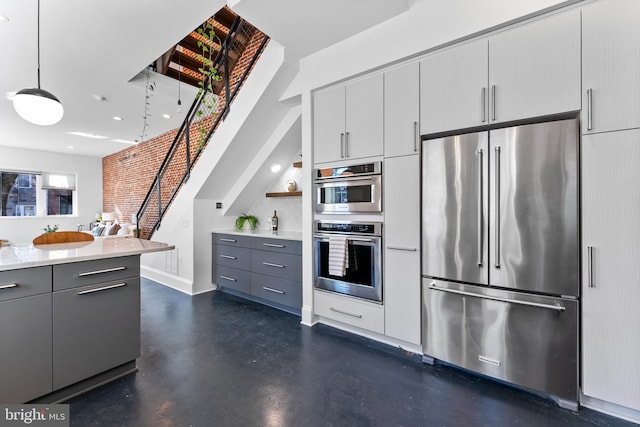 kitchen featuring gray cabinetry, decorative light fixtures, stainless steel appliances, and brick wall