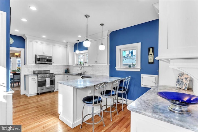 kitchen featuring white cabinetry, appliances with stainless steel finishes, kitchen peninsula, and decorative light fixtures