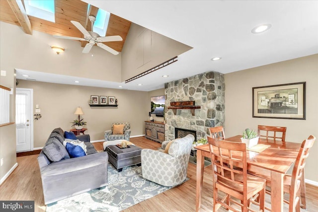 living room featuring ceiling fan, a towering ceiling, a fireplace, and light wood-type flooring