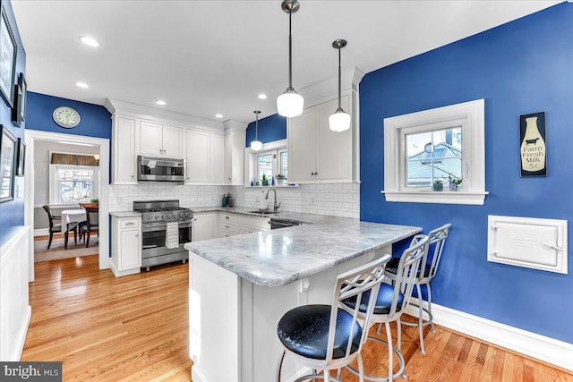 kitchen with white cabinetry, stainless steel appliances, decorative light fixtures, and kitchen peninsula