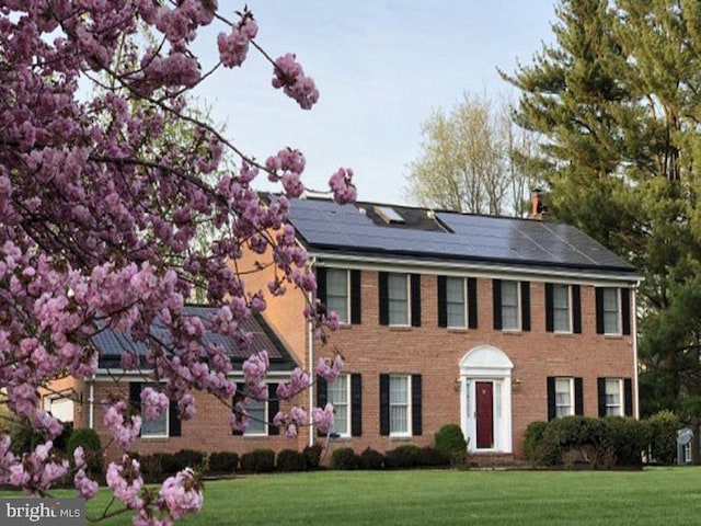 colonial inspired home featuring a front lawn and solar panels