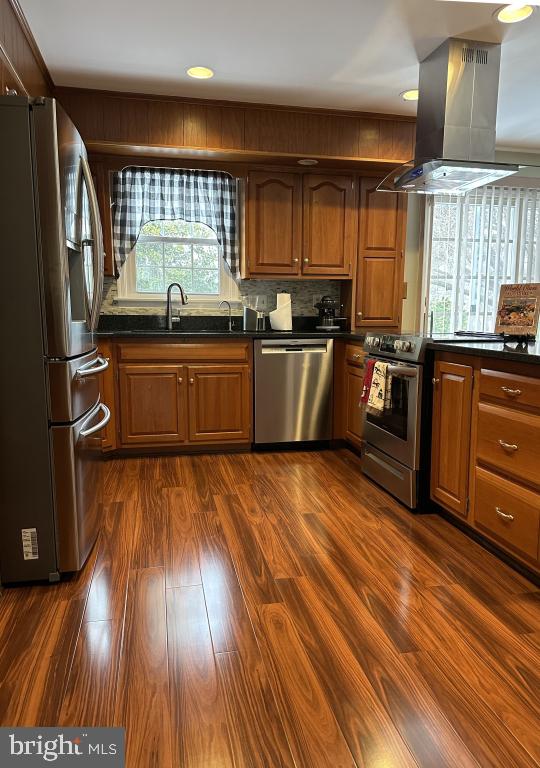 kitchen with appliances with stainless steel finishes, dark hardwood / wood-style floors, island range hood, sink, and backsplash