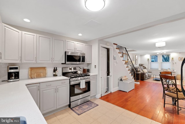 kitchen with decorative backsplash, stainless steel appliances, light hardwood / wood-style floors, and white cabinets