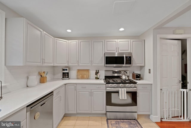 kitchen featuring tasteful backsplash, white cabinetry, stainless steel appliances, and light tile patterned flooring