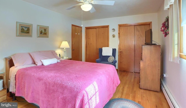 bedroom with two closets, light hardwood / wood-style floors, ceiling fan, and baseboard heating