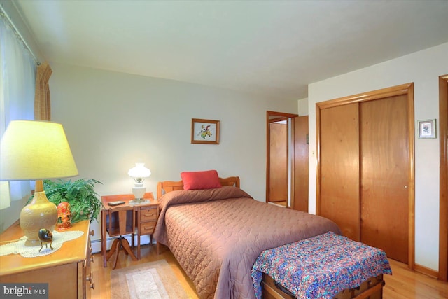 bedroom featuring baseboard heating, light hardwood / wood-style floors, and a closet